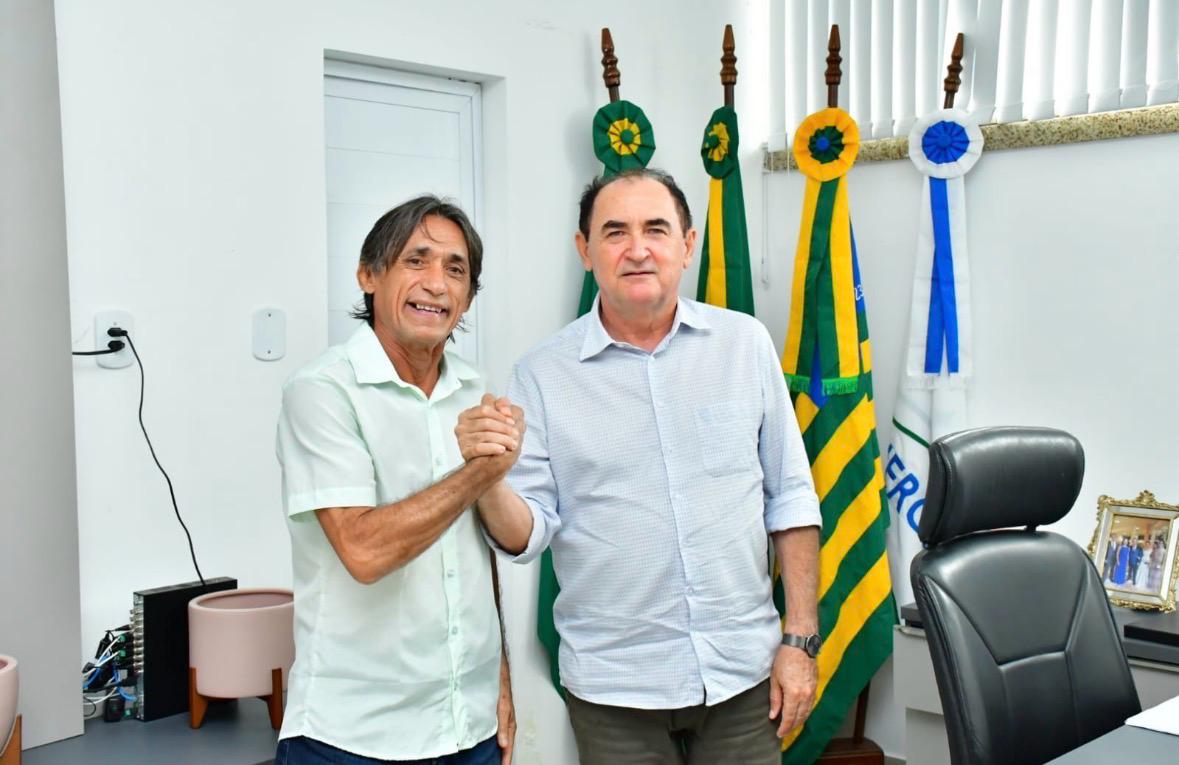 Joaquim Saraiva cumprimenta aliado em reunião, com bandeiras oficiais ao fundo